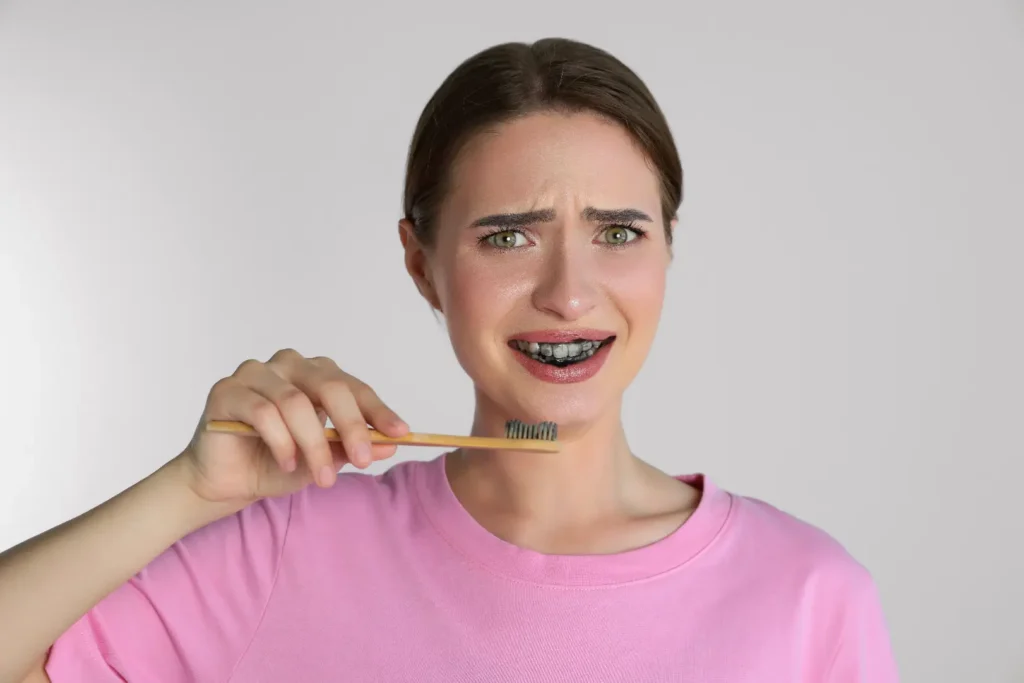 Person holding a toothbrush with a worried expression and visible darkened teeth against a plain background.