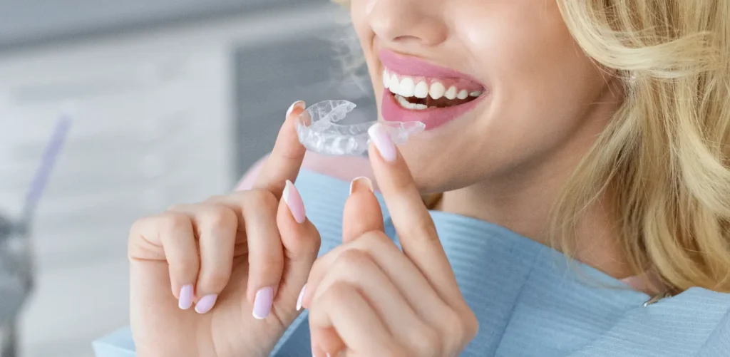 Smiling person holding a clear aligner after removing it from their teeth.